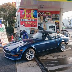 a blue sports car parked in front of a gas station with an attendant working on it