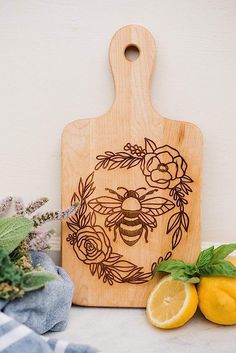 a cutting board with a bee on it next to some lemons and flowers,