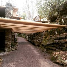 a wooden bridge over a gravel road in front of a stone building and trees on the other side