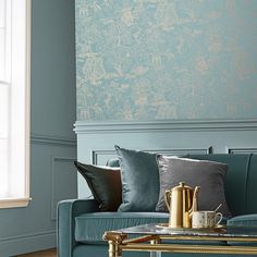 a living room with teal walls and gold accents on the coffee table in front of the couch