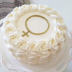 a white cake with gold beads and a cross on top is sitting on a platter