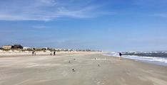 people are walking on the beach near the water and houses in the distance with blue skies