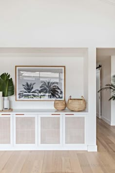 a living room with white walls and wooden floors, two baskets on top of the shelf