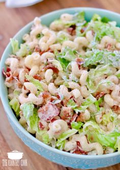 a salad with lettuce and bacon in a blue bowl on top of a table