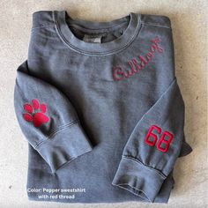 Support your favorite team or player with this custom embroidered Comfort Colors! These sweatshirts are so comfy and will become your go to! They are pigment dyed and have that lived it cozy feel. They wash super well so they will hold up for years! Perfect to pair with leggings this fall.  -Unisex sizing - Collar and sleeve designs are embroidered  - I can do more icons than the paw print. Message me with your idea! - The longer the text, the smaller the font will be. We offer mock ups if requested. Drop down menu explained: First pick your sweatshirt color Next you will pick your size and if you want just the collar or add on sleeves. If you select "Small with Collar & 1" You would get the collar Embroidery plus 1 sleeve Embroidery. Any questions, please message before ordering :) Embroidery School Designs, Sweatshirt Sleeve Designs, Embroidered Team Sweatshirt, Embroidered Sports Sweatshirt, Team Sweatshirts Ideas, Embroidery Sportswear, Embroidery Sweatshirt Ideas, Football Embroidery Designs, Sports Embroidery