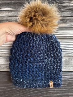 a hand holding a blue knitted hat with a brown pom - pom