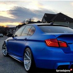 the rear end of a blue car parked in a parking lot next to a house