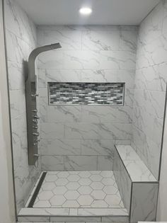 a walk in shower sitting next to a white tiled wall and floor with glass tile