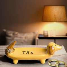 a yellow dog figurine sitting on top of a table next to two gold rings