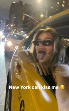 a woman is driving in the back of a yellow car with her mouth open and tongue out