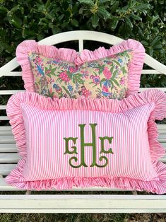 a white bench with pink and green pillows sitting on it's sides next to bushes