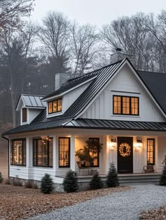 a white house with black shingles and lights on the front door is lit up at night