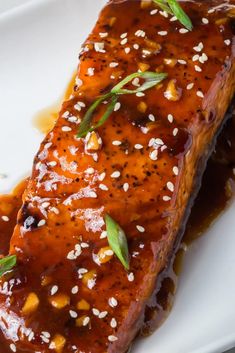 a piece of salmon covered in sauce and garnished with sesame seeds on a white plate