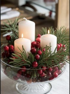 three candles are lit in a glass bowl filled with holly and cranberries on a table