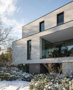 a house with snow on the ground and bushes in front of it, surrounded by trees