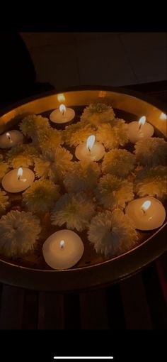 many lit candles in a metal bowl with flowers and leaves on the bottom, surrounded by water