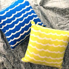 two blue and yellow pillows sitting on top of a bed next to eachother