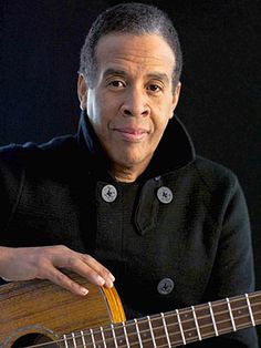 a man holding an acoustic guitar and posing for the camera with his hand on it