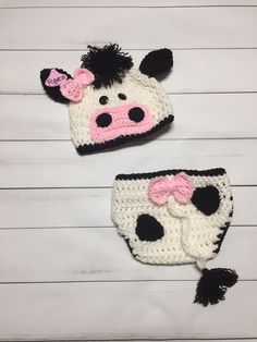 two crocheted cow hats and diaper covers on white wood planks, one is pink and the other is black