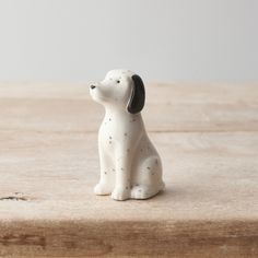 a small white dog figurine sitting on top of a wooden table next to a wall