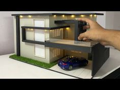 a model house with a car parked in front of it and someone's hand holding the door open