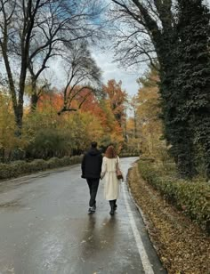 two people are walking down the road in the fall season, holding hands and looking at each other