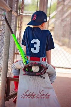 a young boy sitting in the dugout with a baseball bat and glove on his knee