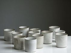 several white cups are lined up on a table with one sitting in the middle and six standing