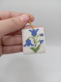 a hand holding a small square beaded keychain with blue flowers on it