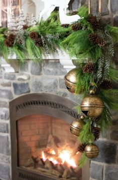 a fireplace decorated for christmas with pine cones and bells