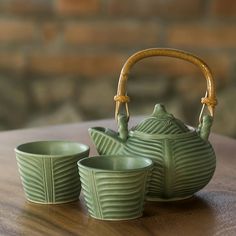 a green tea pot and two cups on a wooden table next to a brick wall