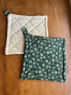 two quilted pot holders sitting on top of a wooden table next to each other