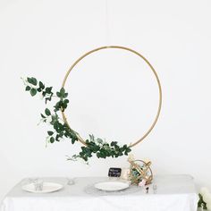 a white table topped with plates and greenery next to a gold circle hanging from the ceiling