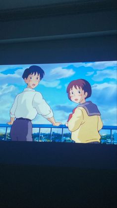 two people standing in front of a large screen with the sky and clouds behind them