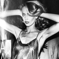 a black and white photo of a woman with her hair blowing in the wind, wearing a shiny dress