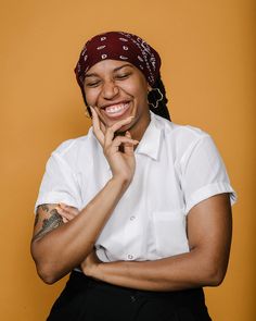 a woman smiling with her hands on her chin and wearing a bandana over her head