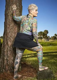 a woman with tattoos is leaning against a tree