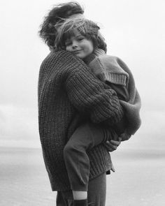 black and white photograph of a woman carrying a child on her back with the ocean in the background