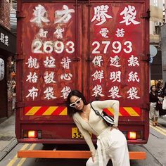 a woman posing in front of a truck with chinese writing on it's side