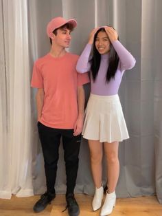 a man and woman standing next to each other in front of a curtain with their hands on their head