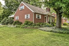 a red brick house sitting in the middle of a lush green yard with trees and bushes