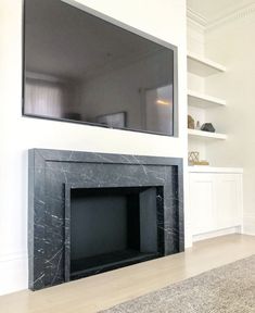 a flat screen tv mounted on the wall above a fireplace in a room with white walls