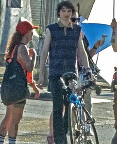 a man standing next to a woman holding an umbrella over her head while on a bike