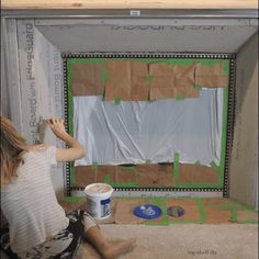 a woman sitting on the floor in front of a wall with cardboard taped to it