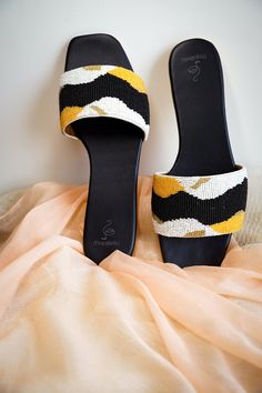 Introducing the Mojabella Handcrafted Slider Sandal in the delightful 'Curiously Cute' design! These sandals feature a sleek black sole and are adorned with beautiful beadwork in black, white, mustard, and yellow hues on the padded strap. The intricate design adds a touch of elegance and uniqueness to these summer-perfect sandals. Comfort is key with the 'Curiously Cute' slider sandals. The padded strap not only showcases a stunning design but also includes padding underneath to prevent toe and Black Open Toe Fabric Sandals, Black Fabric Open Toe Sandals, Rolled Jeans, Comfortable Chic, Slider Sandals, Beach Attire, Beautiful Beadwork, Satin Bags, How To Make Shoes