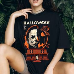 a woman sitting on the ground wearing a black halloween t - shirt