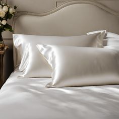 a bed with white sheets and pillows on top of it next to a vase filled with flowers