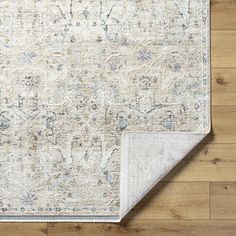 a white rug with blue and gray accents on top of a wooden floor next to a beige area rug