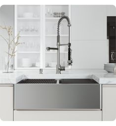 a stainless steel kitchen sink and faucet in front of white cabinets with glass shelves