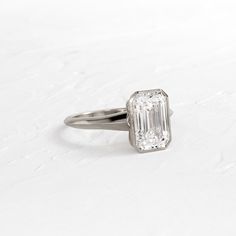 an emerald - cut diamond ring sits on a white surface